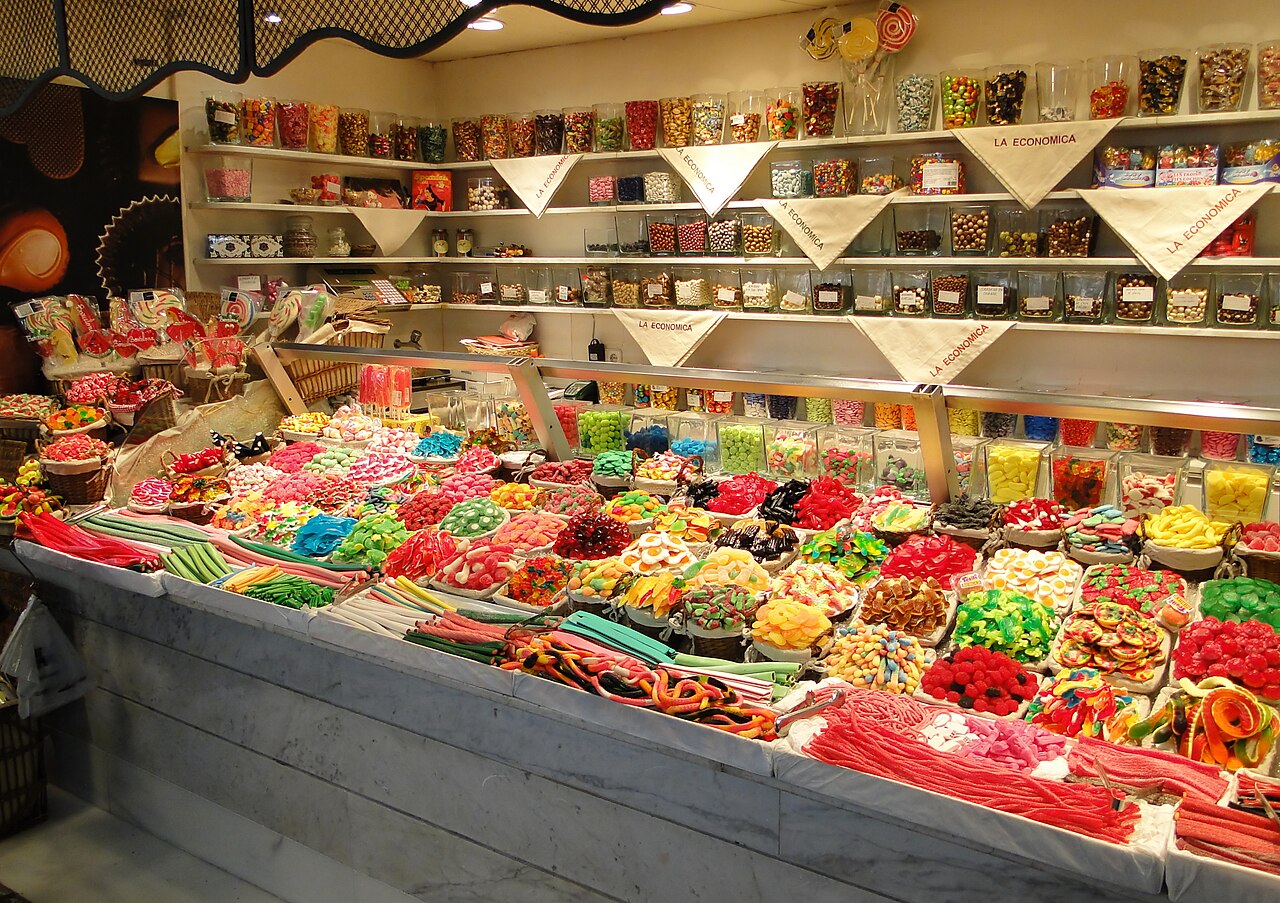 Fruit and juice stalls inside La Boqueria market hall, with hanging price boards