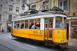 A yellow number 28 tram climbing a narrow Lisbon street between old buildings