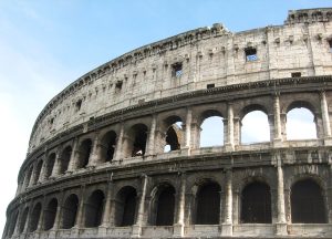 The outer wall of the Colosseum in daylight, with the arched tiers and the modern street level below