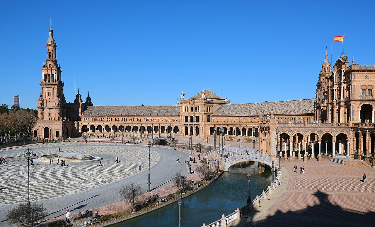 An ornate Mudéjar courtyard with pointed arches, tilework and a long reflecting pool