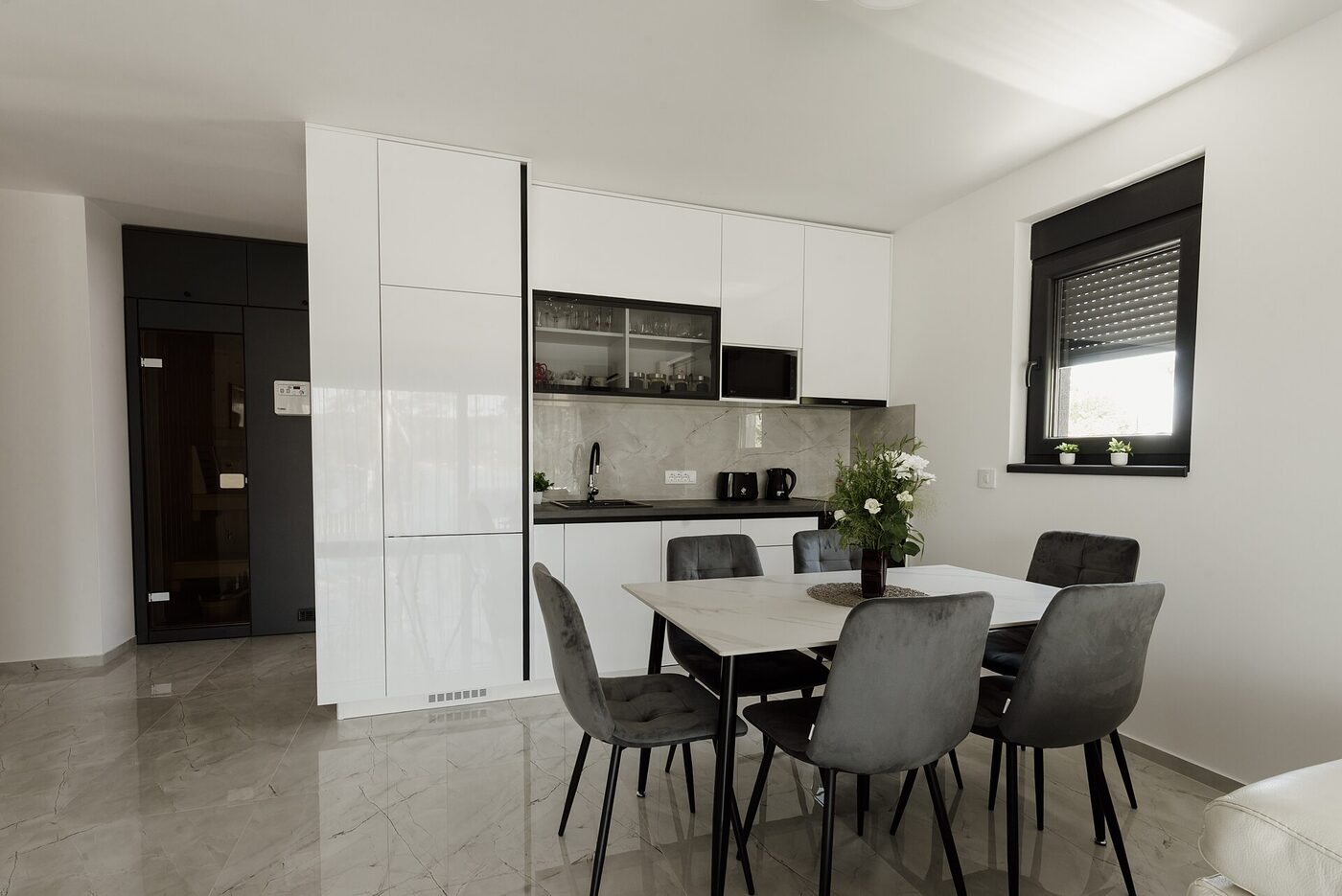 An open-plan apartment interior with a kitchen counter, dining table and living area in daylight