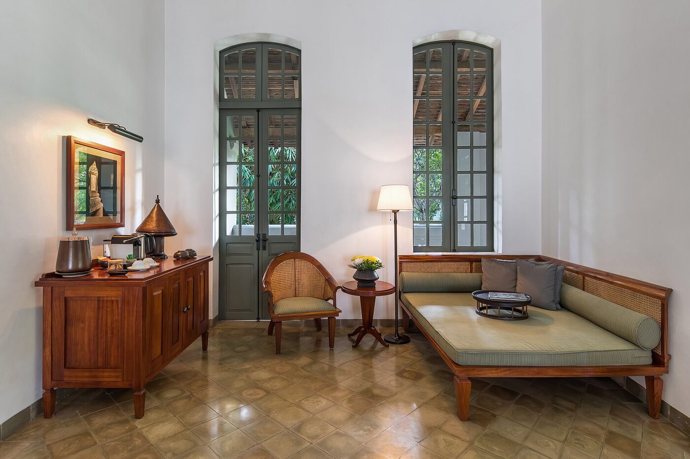 The lounge of a hotel suite with a daybed, tall shuttered windows and a coffee tray on the sideboard