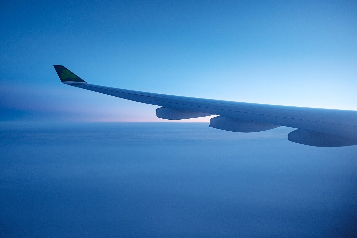 An aircraft wing seen from a window seat, above a bank of cloud lit by low sun