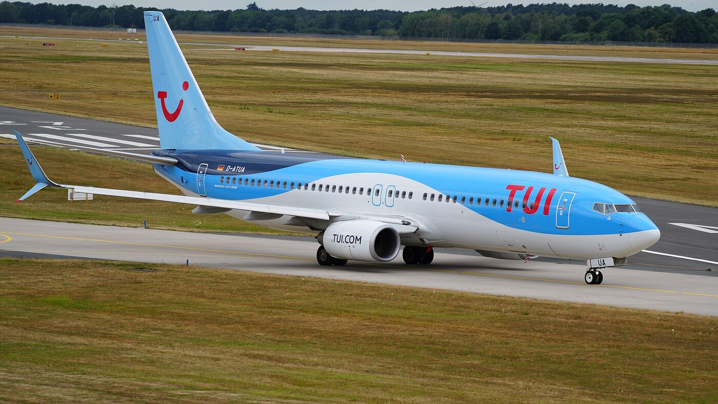 A TUI Boeing 737 in blue and white livery taxiing on a runway past open grass