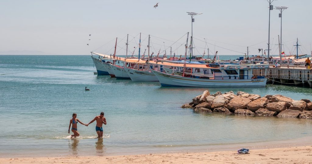 Two people wading in shallow sea water beside moored fishing boats