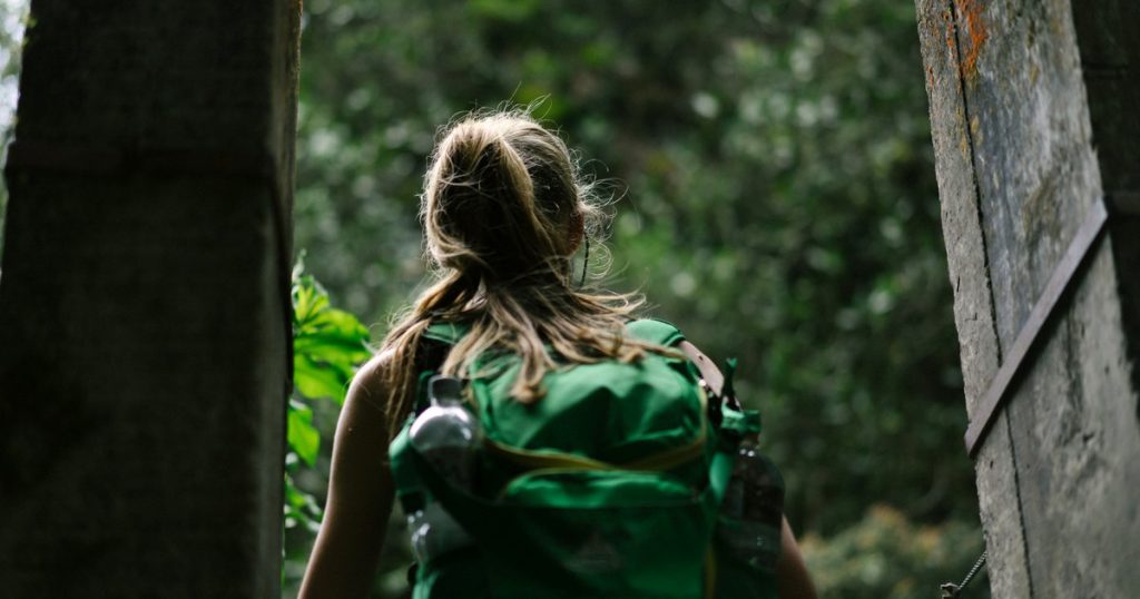 Traveller with a green backpack walking along a shaded forest trail